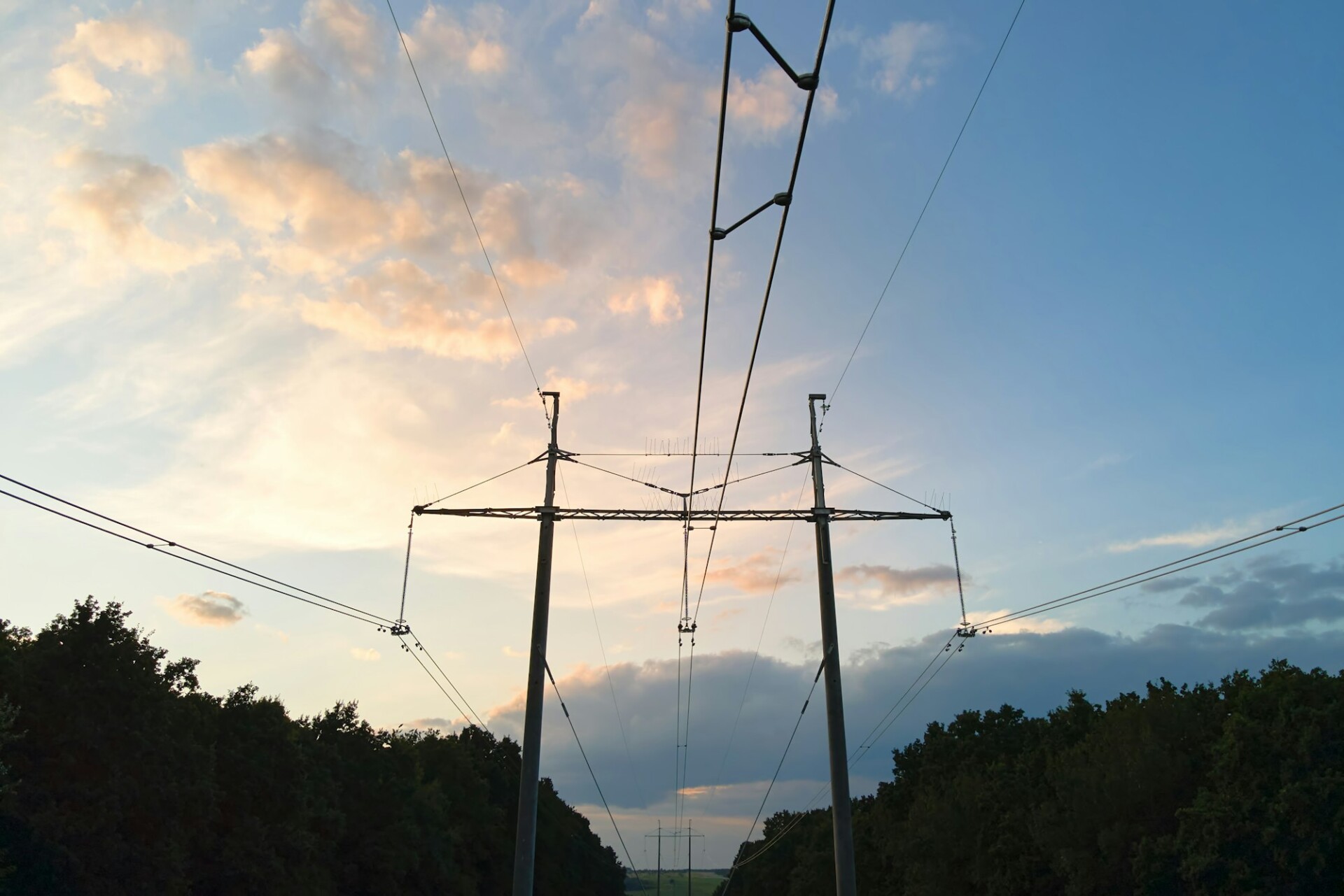 Dunkle Silhouette eines Hochspannungsturms mit Stromleitungen bei Sonnenaufgang.