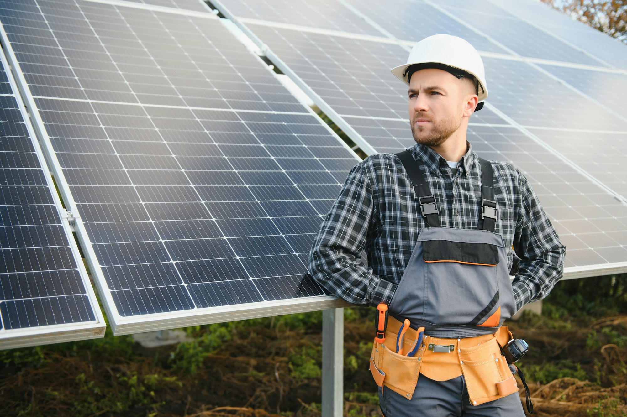 Male worker in uniform outdoors with solar batteries at sunny day.